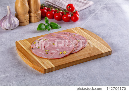 Sliced mortadella with pistachios on wooden cutting board, cherry tomatoes, basil, garlic and salt and pepper grinders in background Sliced mortadella with pistachios on wooden cutting board, cherry tomatoes, basil, garlic and salt and pepper grinders in background 142704170