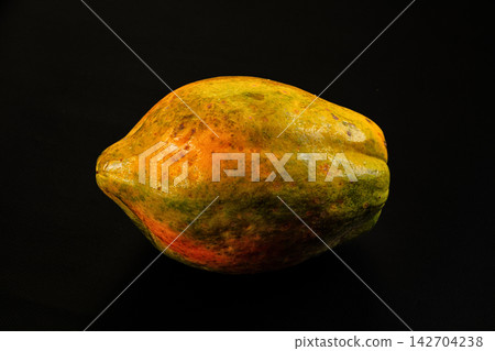 Ripe papaya with yellow green orange skin on black background, shallow depth of field, studio lighting highlighting texture and natural blemishes Ripe papaya with yellow green orange skin on black background, shallow depth of field, studio lighting highlighting texture and natural blemishes 142704238