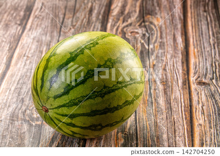 Whole green watermelon with dark stripes resting on rustic wooden surface, natural lighting, shallow depth of field, copy space on right Whole green watermelon with dark stripes resting on rustic wooden surface, natural lighting, shallow depth of field, copy space on right 142704250