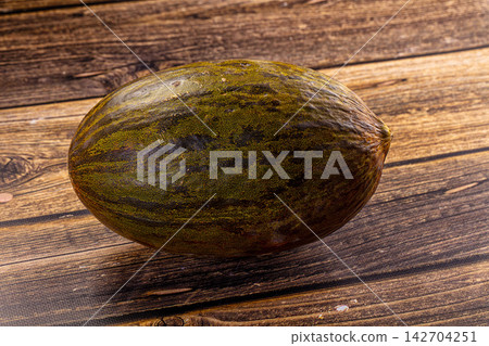 Ripe melon with mottled green and brown rind resting on rustic wooden surface, natural lighting highlights texture and organic imperfections Ripe melon with mottled green and brown rind resting on rustic wooden surface, natural lighting highlights texture and organic imperfections 142704251