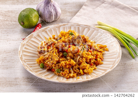 Fried rice with chicken pieces, green peas, red chili, and bean sprouts served on striped ceramic plate with lime, garlic, and spring onions nearby Fried rice with chicken pieces, green peas, red chili, and bean sprouts served on striped ceramic plate with lime, garlic, and spring onions nearby 142704262