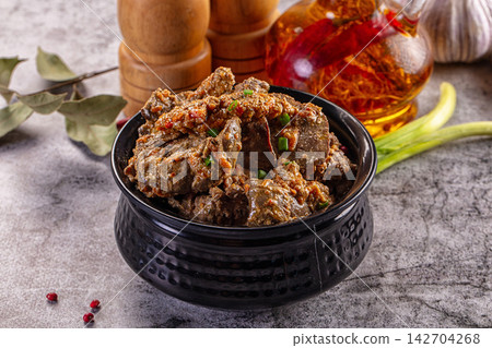 Spiced chicken liver in black textured bowl with green onions, bay leaves, garlic, and chili oil on rustic stone surface 142704268