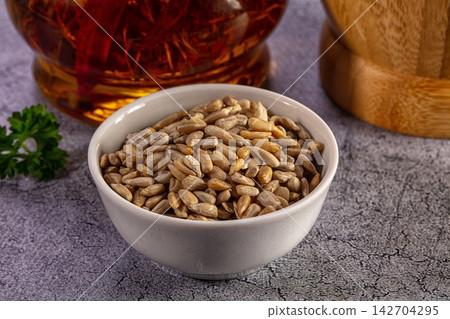 Shelled sunflower seeds in a white ceramic bowl with oil and parsley on a gray table Shelled sunflower seeds in a white ceramic bowl with oil and parsley on a gray table 142704295