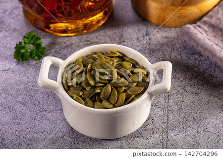 Shelled pumpkin seeds, or pepitas, in a white bowl on a grey textured background Shelled pumpkin seeds, or pepitas, in a white bowl on a grey textured background 142704296