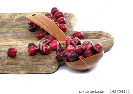 Fresh cranberries in a wooden spoon on a rustic cutting board Fresh cranberries in a wooden spoon on a rustic cutting board 142704331