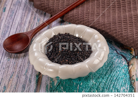 Black sesame seeds in white ceramic bowl with wooden spoon on rustic painted wood surface and brown textile background Black sesame seeds in white ceramic bowl with wooden spoon on rustic painted wood surface and brown textile background 142704351