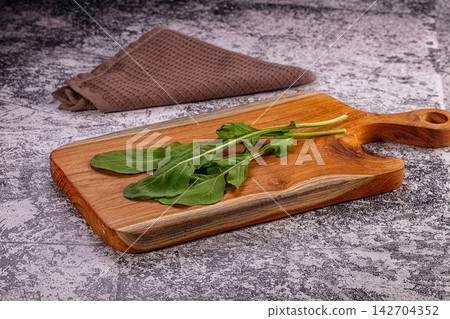 Fresh green dandelion leaves on rustic wooden cutting board with brown waffle weave napkin against textured gray surface Fresh green dandelion leaves on rustic wooden cutting board with brown waffle weave napkin against textured gray surface 142704352
