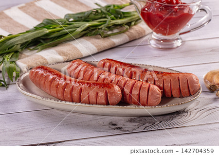 Grilled sausages with diagonal cuts on ceramic plate, fresh green herbs and glass ketchup pitcher on rustic wooden table Grilled sausages with diagonal cuts on ceramic plate, fresh green herbs and glass ketchup pitcher on rustic wooden table 142704359