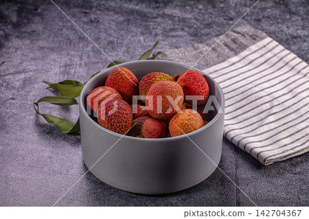 Fresh lychee fruits in gray ceramic bowl with green leaves and striped cloth on dark textured surface Fresh lychee fruits in gray ceramic bowl with green leaves and striped cloth on dark textured surface 142704367