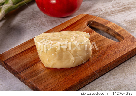 Block of halloumi cheese on wooden cutting board with tomato background Block of halloumi cheese on wooden cutting board with tomato background 142704383