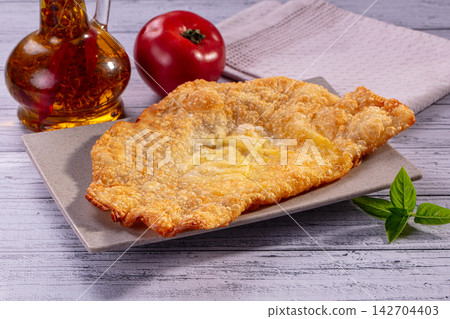 Golden fried cheburek on square plate with fresh tomato, basil leaves and oil bottle on rustic white wood background 142704403