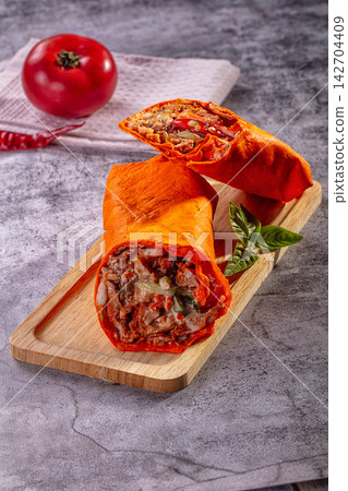Chicken shawarma wrap cut in half on wooden board with fresh tomato and basil, vibrant orange tortilla, rustic gray background Chicken shawarma wrap cut in half on wooden board with fresh tomato and basil, vibrant orange tortilla, rustic gray background 142704409