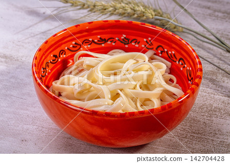 Udon noodles in vibrant red ceramic bowl with black and white decorative pattern, set on textured surface with wheat stalks in background Udon noodles in vibrant red ceramic bowl with black and white decorative pattern, set on textured surface with wheat stalks in background 142704428