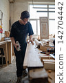 Thoughtful master carpenter checking surface of wooden frame after processing detail with hand plane 142704442