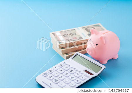 一個粉紅色的小豬存錢罐，一個白色計算器，還有一疊鈔票。 142704917