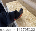 A Close-Up of a Person Holding a Power Tool, Preparing to Work with Plywood in a Crafting or Construction Environment 142705122