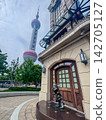 A whimsical bronze statue of a cartoon mouse stands in front of a classic building, overlooking the iconic tower piercing the skyline in a bustling urban environment. 142705127