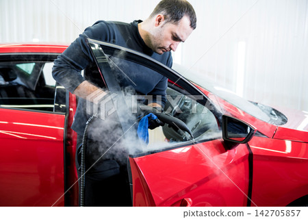 Car service worker cleans interiror with steam cleaner Car service worker cleans interiror with steam cleaner 142705857