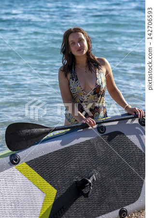 Smiling woman standing with paddleboard on sunny ocean beach Smiling woman standing with paddleboard on sunny ocean beach 142706593