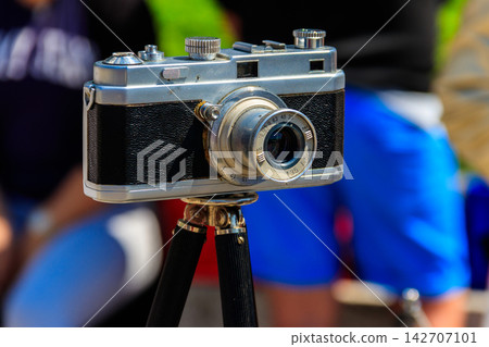 Retro photo camera on tripod on a street Retro photo camera on tripod on a street 142707101