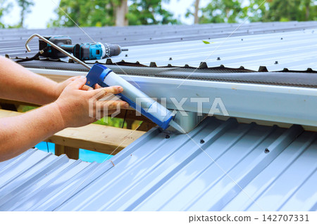 Man applying sealant on metal roof during construction work Man applying sealant on metal roof during construction work 142707331