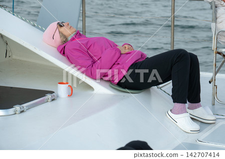 Woman rests and sleeps on catamaran deck while experiencing seasickness and drowsiness after taking motion sickness medication. Travel health, medication side effect, fatigue and marine journey 142707414