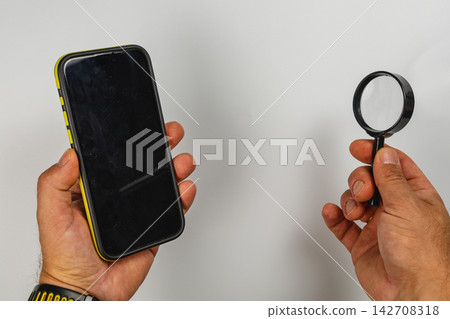 Using a magnifying glass to inspect a smartphone in a bright space Using a magnifying glass to inspect a smartphone in a bright space 142708318