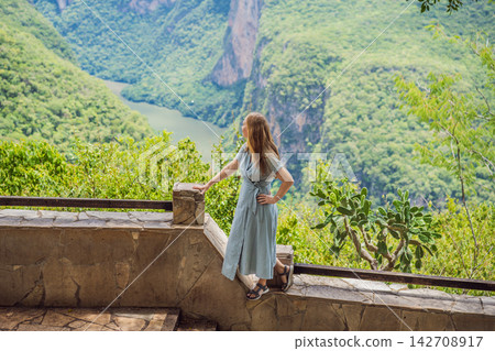 Woman tourist admiring the dramatic Sumidero Canyon viewpoint in Chiapas Mexico with steep canyon walls lush landscape river overlook nature tourism and looking across the canyon. Woman tourist admiring the dramatic Sumidero Canyon viewpoint in Chiapas Mexico with steep canyon walls lush landscape river overlook nature tourism and looking across the canyon. 142708917