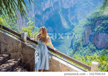 Woman tourist admiring the dramatic Sumidero Canyon viewpoint in Chiapas Mexico with steep canyon walls lush landscape river overlook nature tourism and admiring the river landscape. Woman tourist admiring the dramatic Sumidero Canyon viewpoint in Chiapas Mexico with steep canyon walls lush landscape river overlook nature tourism and admiring the river landscape. 142709143