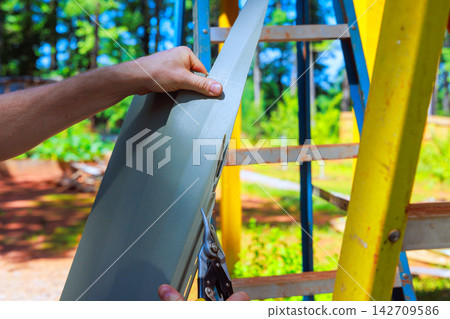 Cutting piece of PVC siding sheet on ladder in backyard Cutting piece of PVC siding sheet on ladder in backyard 142709586