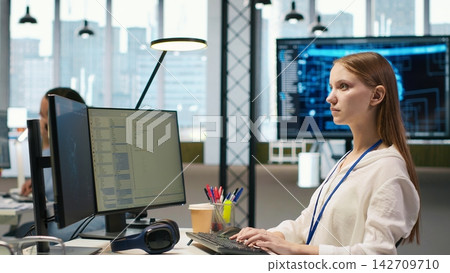 Female technician coding with AI language model assistance in startup office, using PC. Intern using computer, integrating artificial intelligence LLM assistant suggestions into code editor, camera A Female technician coding with AI language model assistance in startup office, using PC. Intern using computer, integrating artificial intelligence LLM assistant suggestions into code editor, camera A 142709710