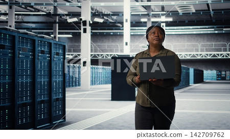 Data center engineer using laptop to develop disaster recovery plans, minimizing downtime. Server farm IT expert enhancing data protection protocols using notebook, camera A Data center engineer using laptop to develop disaster recovery plans, minimizing downtime. Server farm IT expert enhancing data protection protocols using notebook, camera A 142709762