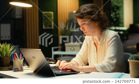 Woman in a dark office after hours leaning back in her office chair, meditating in a calm casual state. Relaxed pose and empowered expression reflect fulfillment of career goals. Camera B. Woman in a dark office after hours leaning back in her office chair, meditating in a calm casual state. Relaxed pose and empowered expression reflect fulfillment of career goals. Camera B. 142709771