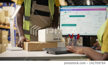 African american woman scanning the barcodes for shipment details on boxes, registering the airway bill data on a package tracking software with accurate parcel updates. Scanner tech. Camera A. African american woman scanning the barcodes for shipment details on boxes, registering the airway bill data on a package tracking software with accurate parcel updates. Scanner tech. Camera A. 142709784