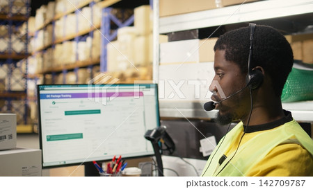 Male call center clerk assisting a person with order mix up problems, verifying parcel status on package tracking software in the warehouse facility. Customer service dispatch support. Camera A. Male call center clerk assisting a person with order mix up problems, verifying parcel status on package tracking software in the warehouse facility. Customer service dispatch support. Camera A. 142709787