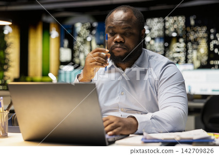 African american staff member distraught thinking about new ideas to impress the board, creating a presentation to help with development. Male reflecting about his decisions and pushing limits. African american staff member distraught thinking about new ideas to impress the board, creating a presentation to help with development. Male reflecting about his decisions and pushing limits. 142709826
