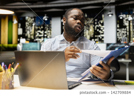 Businessman in workspace staying after hours to focus on budgeting tasks, scheduling the next phase of project development. Ensuring task alignment with the business objectives. Businessman in workspace staying after hours to focus on budgeting tasks, scheduling the next phase of project development. Ensuring task alignment with the business objectives. 142709884