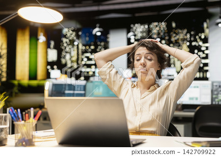 Demotivated businesswoman, sighing, pushing limits, late at night, being in a mental haze and troubled by workload and life choices. Uninterested tensed woman struggling with fatigue. Demotivated businesswoman, sighing, pushing limits, late at night, being in a mental haze and troubled by workload and life choices. Uninterested tensed woman struggling with fatigue. 142709922