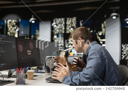 Software developer at office desk thinking how to fix critical error warning displayed on computer. Tech startup IT worker brainstorming how to fix computer bug affecting server network Software developer at office desk thinking how to fix critical error warning displayed on computer. Tech startup IT worker brainstorming how to fix computer bug affecting server network 142709948