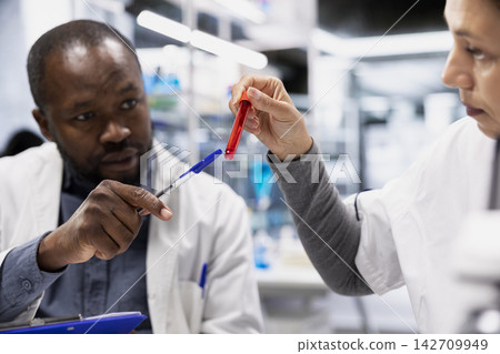 Team of scientists analyzing blood samples for hereditary disease markers. Teamworking laboratory coworkers doing research on sanguine fluid vials to identify genetic predisposition risks, camera A Team of scientists analyzing blood samples for hereditary disease markers. Teamworking laboratory coworkers doing research on sanguine fluid vials to identify genetic predisposition risks, camera A 142709949