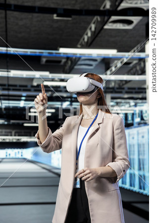 Data center engineer using VR headset gear to coordinate backups and recovery protocols. Server farm employee using virtual reality technology to upgrade equipment components with notebook Data center engineer using VR headset gear to coordinate backups and recovery protocols. Server farm employee using virtual reality technology to upgrade equipment components with notebook 142709989
