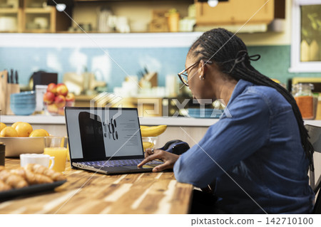 Casual black woman looking at new phone product announcement on laptop, interest and curiosity for new technology on gadget. High tech release coming soon, innovative technology news. Casual black woman looking at new phone product announcement on laptop, interest and curiosity for new technology on gadget. High tech release coming soon, innovative technology news. 142710100