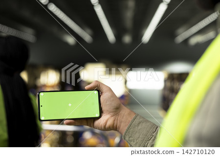 Green screen phone with staff working in warehouse storage facility, coordinating loading and unloading processes with coworker. Shipping operations and order fulfillment in stock industry. Green screen phone with staff working in warehouse storage facility, coordinating loading and unloading processes with coworker. Shipping operations and order fulfillment in stock industry. 142710120