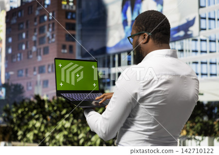 Isolated mockup on pc held by african american man on city center streets, busy metropolitan area full of skyscrapers and dynamic activity. Casual adult walking around downtown avenue. Isolated mockup on pc held by african american man on city center streets, busy metropolitan area full of skyscrapers and dynamic activity. Casual adult walking around downtown avenue. 142710122