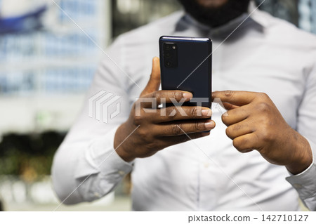 Black person checking his smartphone apps on a metropolitan street, offering candid look at modern lifestyle and dynamic interaction between pedestrian motion and city architecture. Black person checking his smartphone apps on a metropolitan street, offering candid look at modern lifestyle and dynamic interaction between pedestrian motion and city architecture. 142710127