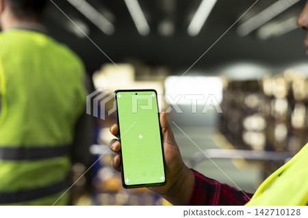 Vertical chroma key, mobile phone, industrial warehouse, staff does package handling, inventory storage management and shipping operations. High visibility vest during logistics planning. Vertical chroma key, mobile phone, industrial warehouse, staff does package handling, inventory storage management and shipping operations. High visibility vest during logistics planning. 142710128
