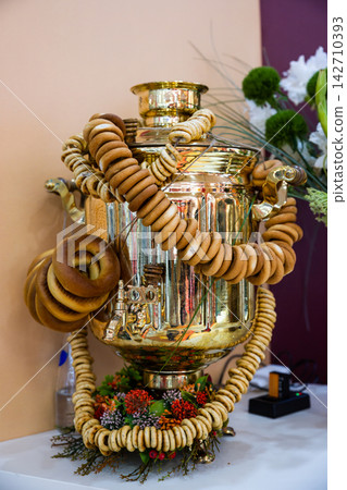 Traditional brass russian samovar decorated with strings of sushki and bubliki rings for tea ceremony celebration close up Traditional brass russian samovar decorated with strings of sushki and bubliki rings for tea ceremony celebration close up 142710393
