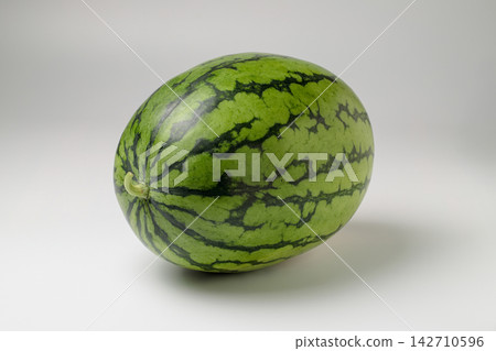 A small, oval-shaped watermelon placed diagonally against a white background. A small, oval-shaped watermelon placed diagonally against a white background. 142710596