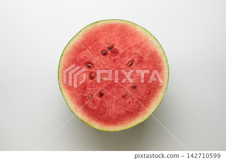 A top-down photograph of the cross-section of a small watermelon cut in half, against a white background. A top-down photograph of the cross-section of a small watermelon cut in half, against a white background. 142710599