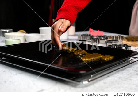 Hand arranging homemade cookies on baking tray beside metal cutters, festive holiday baking, pastry preparation, Christmas cooking, dessert making and seasonal kitchen tradition Hand arranging homemade cookies on baking tray beside metal cutters, festive holiday baking, pastry preparation, Christmas cooking, dessert making and seasonal kitchen tradition 142710660